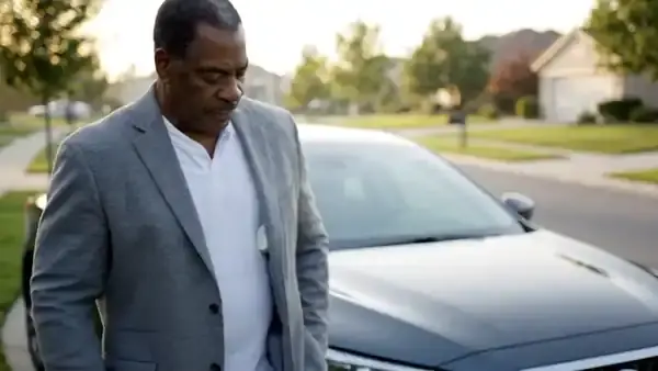 A man in his sixties taking a small white spray bottle out of his jacket pocket beside his car